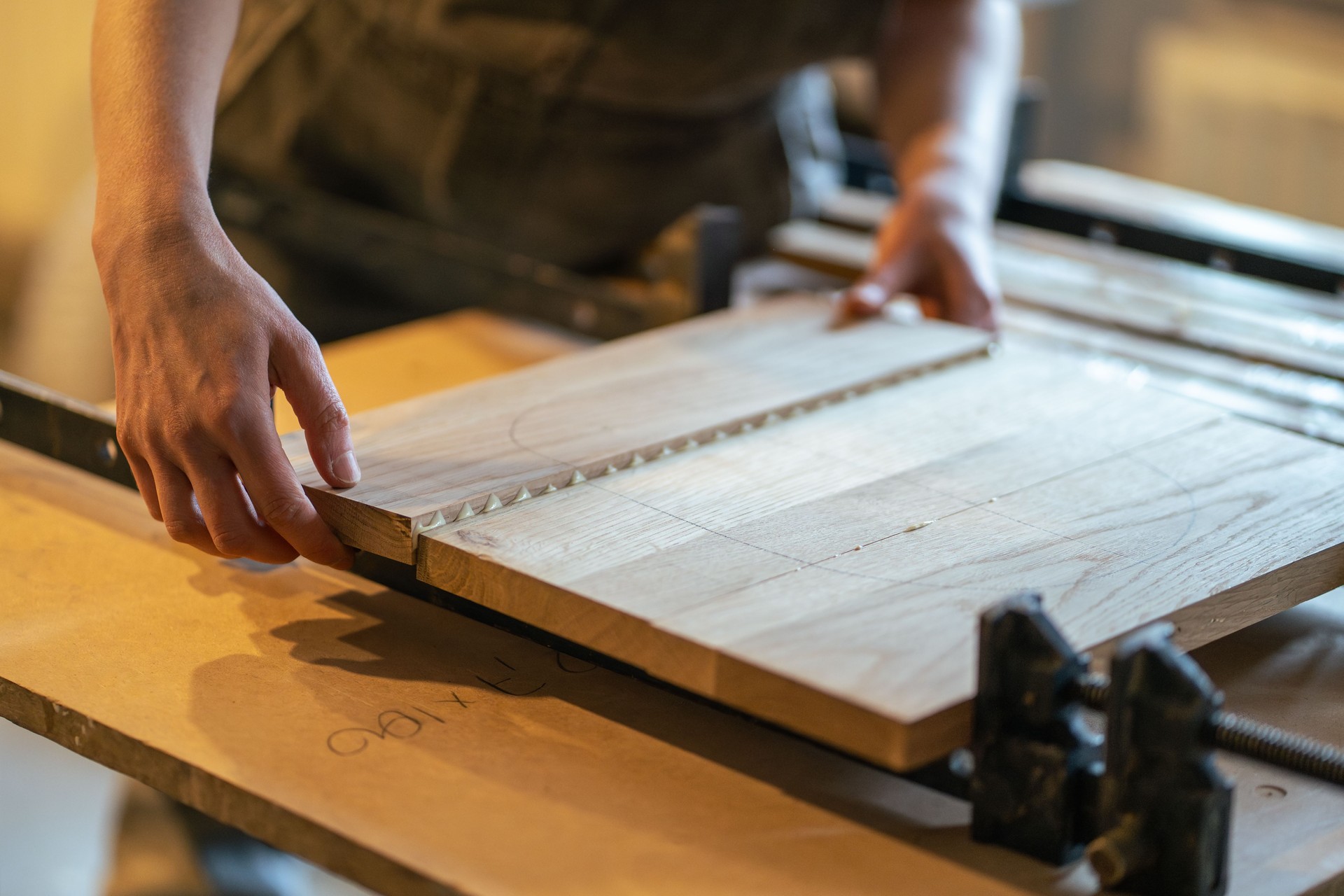 Joiner hands hold glued tabletop, clamp boards in one piece with clamps in furniture workshop